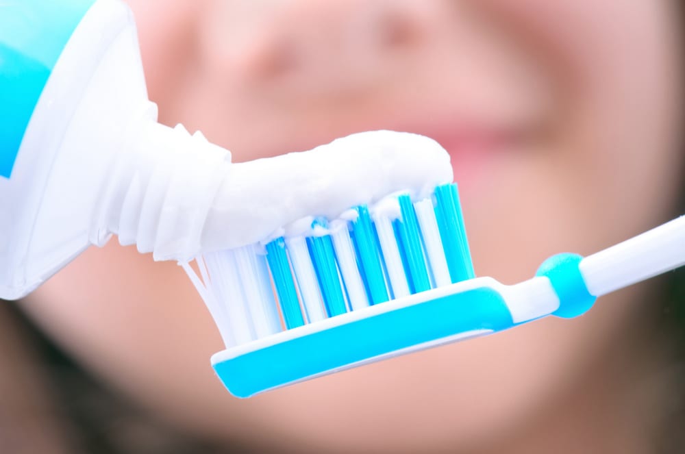 Toothpaste being placed onto a blue and white toothbrush