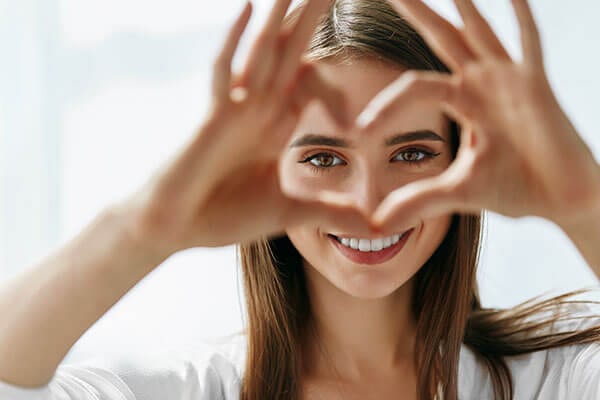 Smiling woman holding fingers up in heart shape to frame her eyes